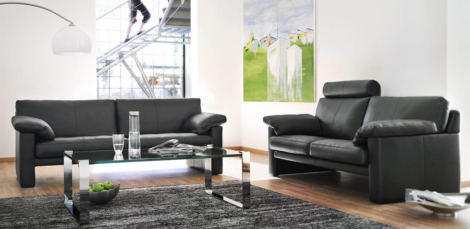 Two CL300 sofas in black leather with armrest cushions, headrest and matching glass table in modern, multi-level living room.