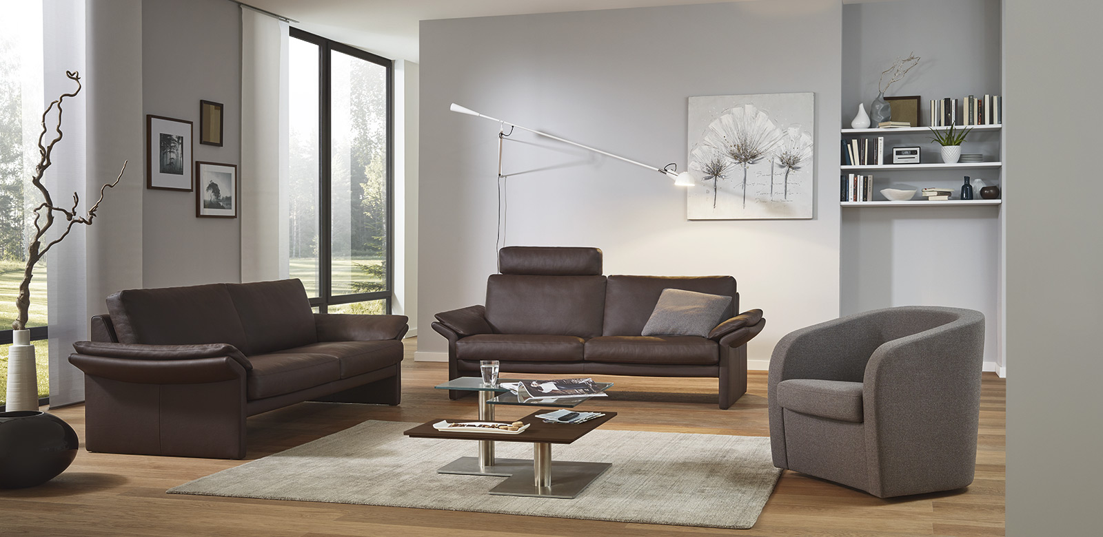 Twee CL910 banken in bruin leer en fauteuils in grijze stof in een moderne woonkamer en terras met uitzicht op het grote pand