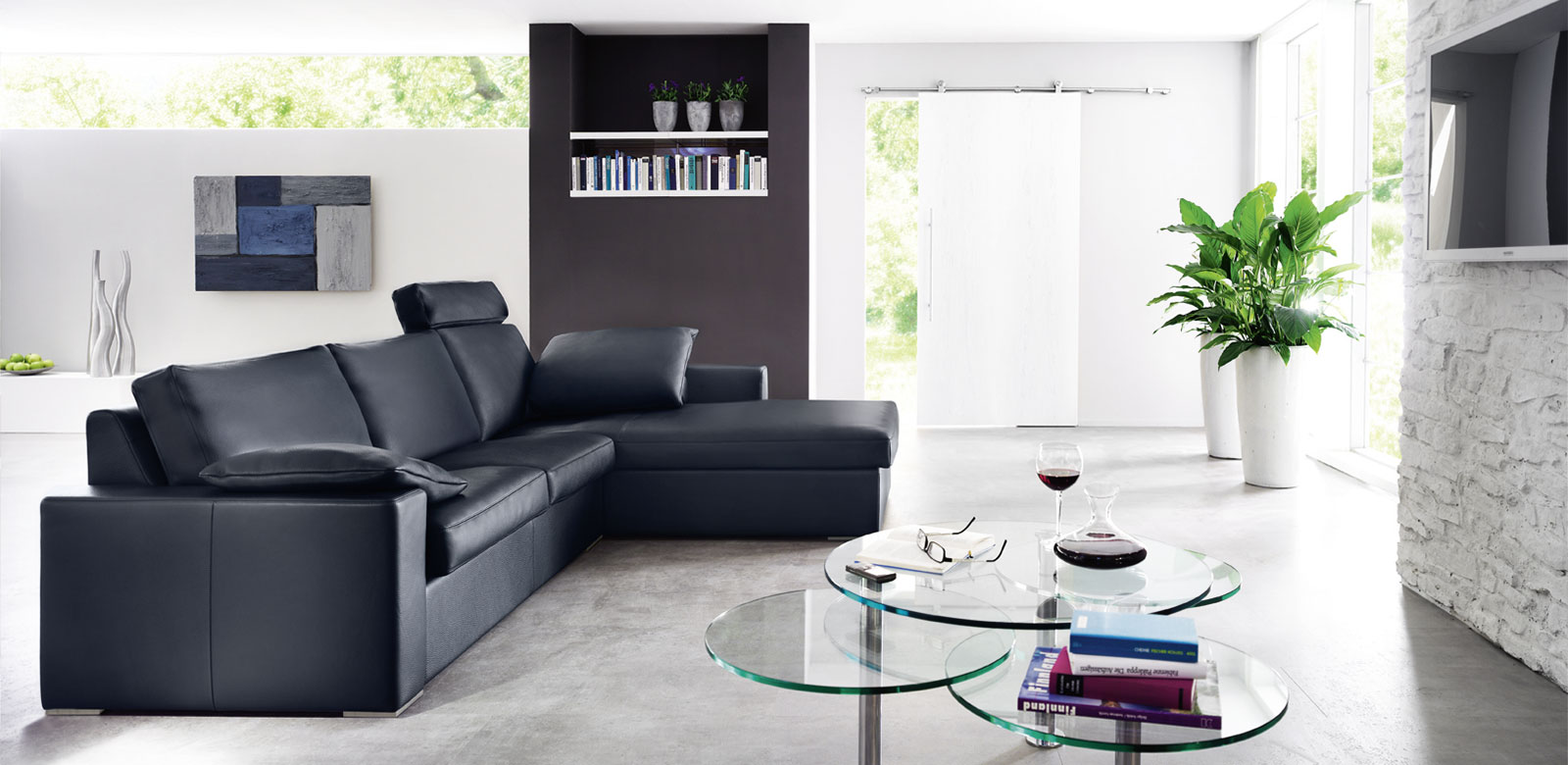 Zijaanzicht CL150 in zwart leer als fauteuilcombinatie met kussens en hoofdsteunen in moderne woonkamer met glazen tafels.