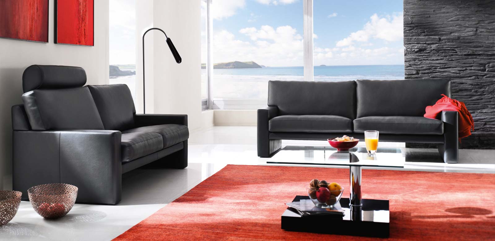 Zwei Sofas CL200 in schwarzem Leder mit Kopfstütze in moderner Strandvilla mit roten und schwarzen Akzenten an Teppichen und Wänden.